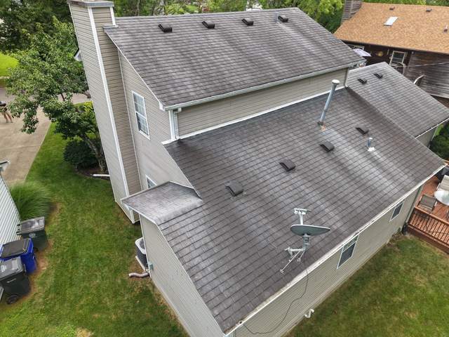 Before: rear of a two-story vinyl-sided home from above, worn gray roof with many box vents