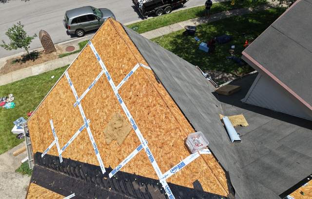 Drone view of a stripped roof slope: bare OSB deck sheets with tape over every seam between sheets; the next slope is already covered in underlayment