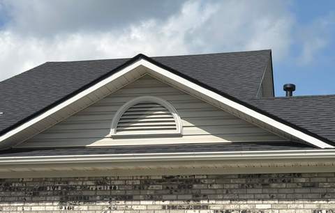 Finished gable and ridge line on the new roof above a vinyl-sided gable with a half-round vent